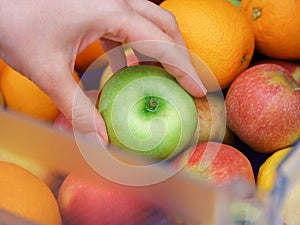 A woman taking a green apple out of a fridge compartment