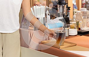 Woman taking iced coffee in a take away cup from cafe counter.