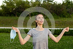 Woman taking of medical mask from face and breathing deeply standing outdoors.