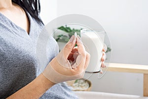 Woman taking medicine with glass of milk and paracetamol pill in hand