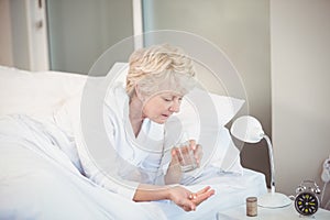 Woman taking medicine while resting on bed