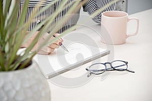 Woman taking notes with a a cup of tea and her reading glasses next to her