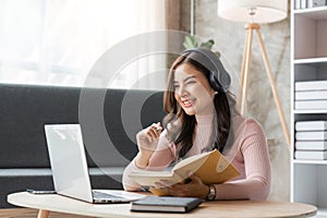 woman taking notes in notebook while using laptop at home in living room. Focused lady writing in notepad