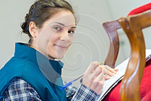 woman taking notes while upholstering chair in workshop