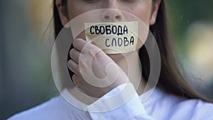 Woman taking off tape with freedom of speech phrase in russian over mouth