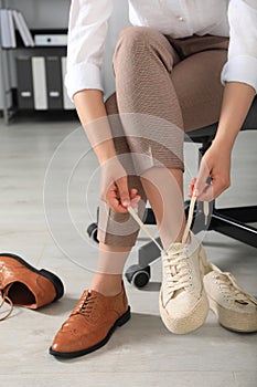 Woman taking off uncomfortable shoes and putting on sneakers in office, closeup