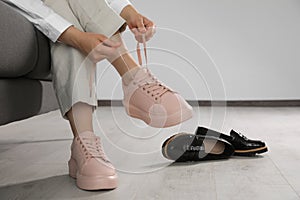 Woman taking off uncomfortable shoes and putting on sneakers in office, closeup