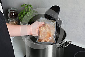 Woman taking out vacuum packed meat from pot in kitchen, closeup. Thermal immersion circulator for sous vide cooking