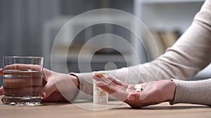 Woman taking painkiller medicine, holding glass of water, closeup of hands