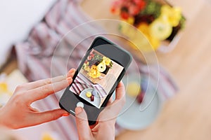 Woman taking photo of flowers and macaroons with smartphone. Instagram photography blogging workshop concept. A girl