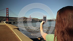 Woman taking photo of Golden Gate Bridge with smartphone