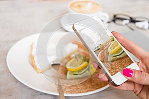 Woman taking photo of her cake in cafe with mobile phone