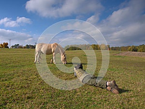 Woman taking photo of nice grazing horse on meadow