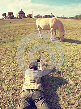 Woman taking photo of nice grazing horse on meadow