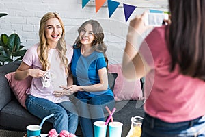 woman taking photo with smartphone of smiling friends with baby shoes