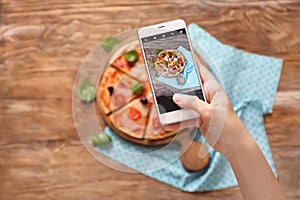 Woman taking photo of tasty pizza with mobile phone, top view