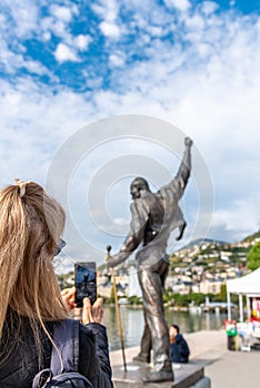 Woman taking a photograph of a statue of Freddie Mercury on the shores of a lake