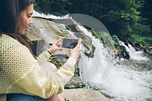 Woman taking picture on the phone of waterfall on background
