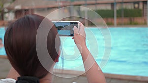Woman taking picture by smartphone of resort swimming pool.