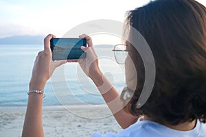 Woman taking pictures of beach, sea and resort at sunrise He used his phone to take high-angle shots. Travel concept and