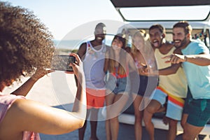 Woman taking pictures of her friends with mobile phone near camper van at beach