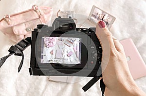 Woman taking pictures with a pen, camera, notebook, bag, and mobile phone on a pink fabric surface