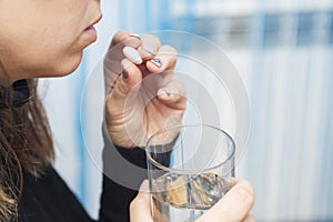 A woman is taking a pill. Females hands are holding one tablet and glass of water close up. Medicine and healthcare concept