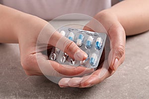 Woman taking pill out from blister pack at grey table, closeup