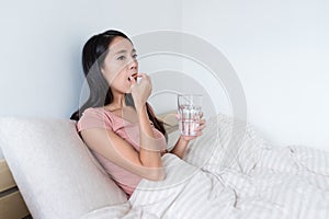 Woman taking pills and drink of water on bed
