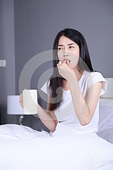 Woman taking pills and drink of water on bed in bedroom