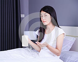 Woman taking pills and drink of water on bed in bedroom