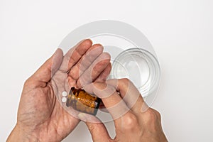 Woman taking pills, female hands with pills from glass bottle and a glass of water on white table