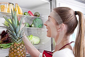 Woman is taking pineapple from her open fridge.