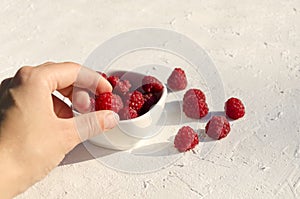 Woman taking raspberry from the bowl.Fresh and ripe fruit on the white surface