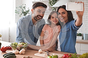 Woman taking selfie with her family on the smartphone in the kitchen