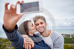 Woman taking selfie while kissing her boyfriend on his cheek