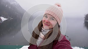 Woman taking selfie and smiling at Ritsa lake in Abkhazia. Snowy day in winter.