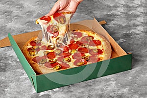 Female hand taking slice of pizza with melted cheese, pepperoni and jalapeno from cardboard box