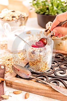 Woman is taking a spoon of Granola, yogurt, nuts and berries