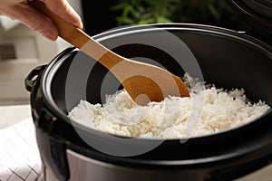 Woman taking tasty rice with spoon from cooker in kitchen