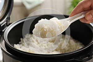 Woman taking tasty rice with spoon from cooker in kitchen