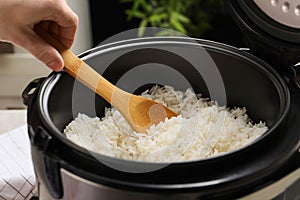 Woman taking tasty rice with spoon from cooker in kitchen