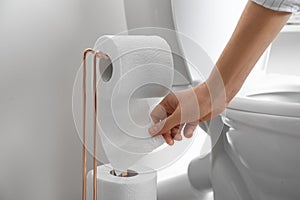 Woman taking toilet paper from roll holder in bathroom, closeup