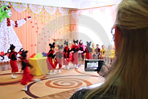 Woman taking video of children`s morning party. Children on matinee at kindergarten