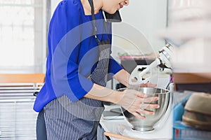 Woman talking on cell phone while using mixer standing in kitchen.