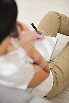 Woman talking cell phone and writing in notepad