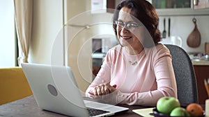 Woman talking in front of laptop screen and sitting at table in home office.