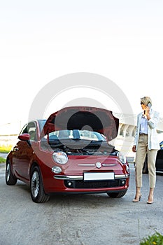 Woman talking on mobile phone asking for help beside her breakdown car