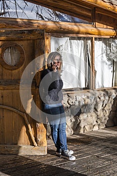 Woman talking on mobile phone leaning against the door of a log cabin