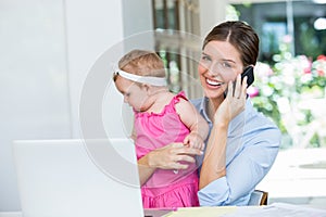 Woman talking on mobile phone while sitting with baby girl